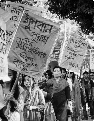 Indigenous women walking in procession with hand-painted cloth banners lettered in Bengali.